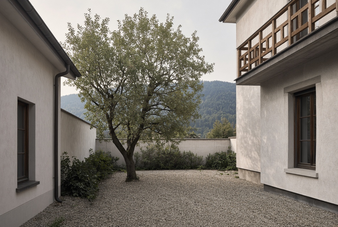 Ruhiger Innenhof mit Kies, einem Baum und hellen Fassaden